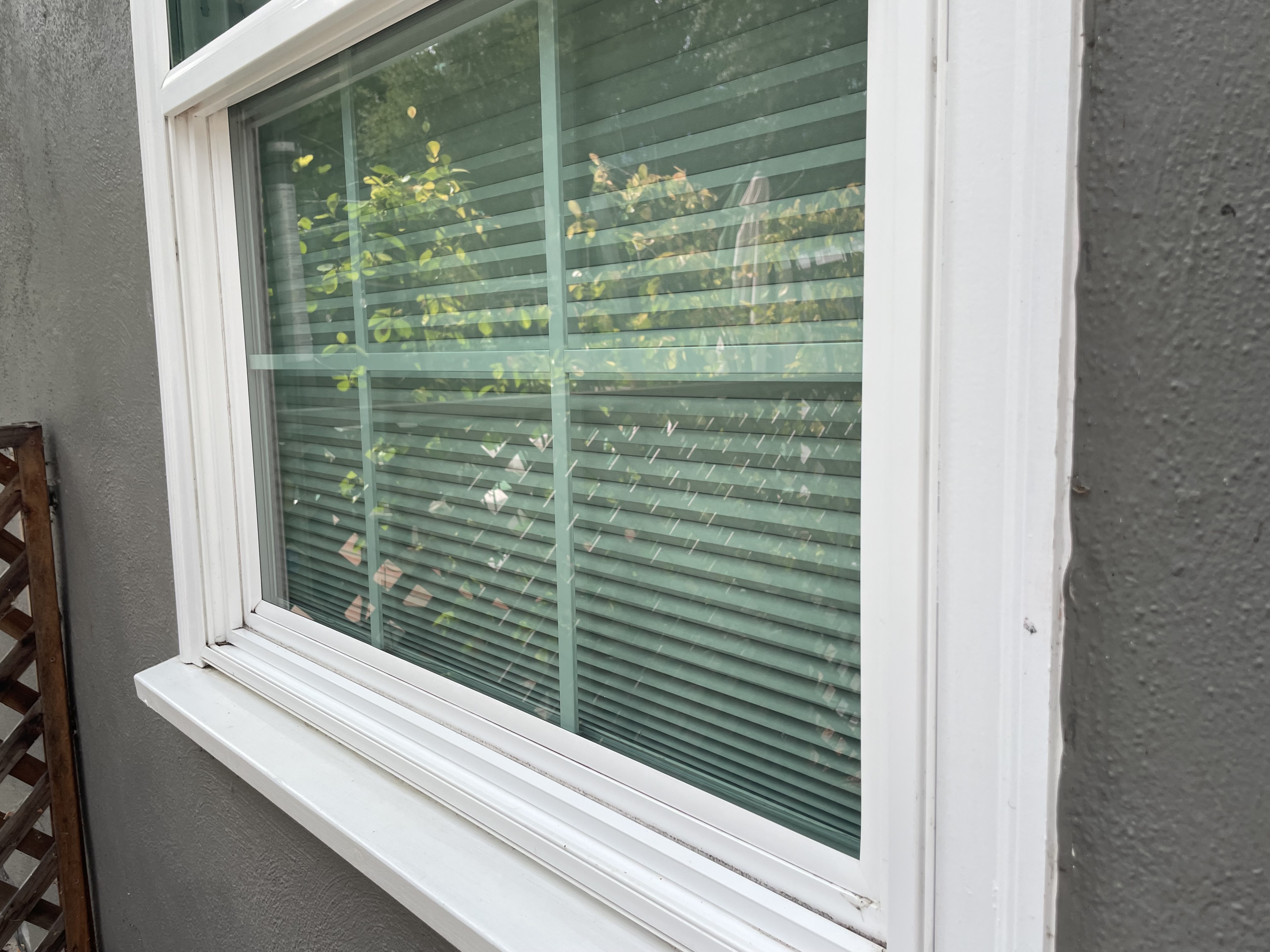 Residential window with water spots, streaks, and dirt buildup on glass and blinds